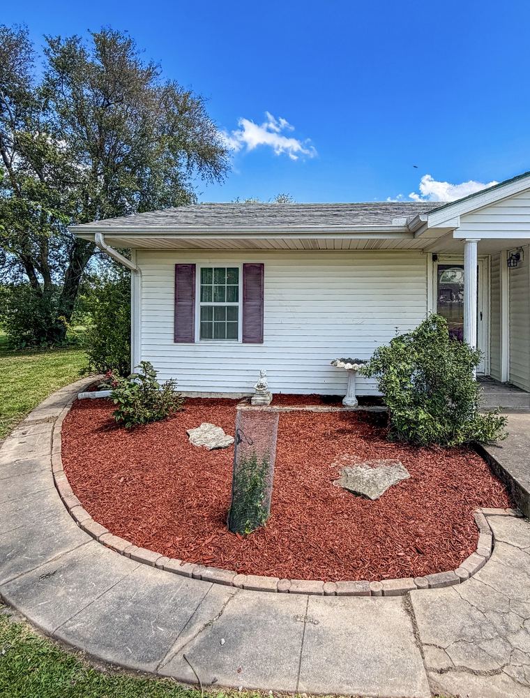 Circular landscape bed with red mulch, birdbath, and stone accents